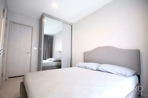 Condominium for rent in Khlong Toei, Bangkok - Second bedroom with upholstered headboard, sliding mirrored wardrobe and neutral walls.
