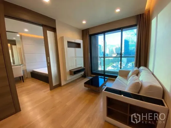 Condominium for rent in Bang Rak, Bangkok - Living room with wall-mounted TV unit, sliding door to bedroom and city view.
