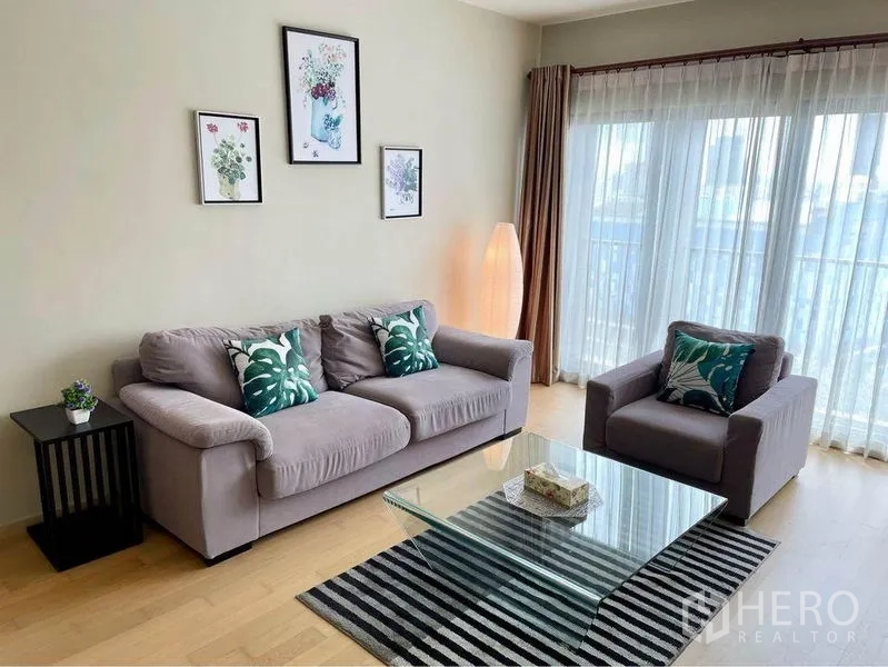 คอนโด ให้เช่าในWatthana, Bangkok - ห้องนั่งเล่นรับแสงธรรมชาติ โซฟาสีเทา อาร์มแชร์ โต๊ะกลางกระจก และประตูกระจกเปิดสู่ระเบียง