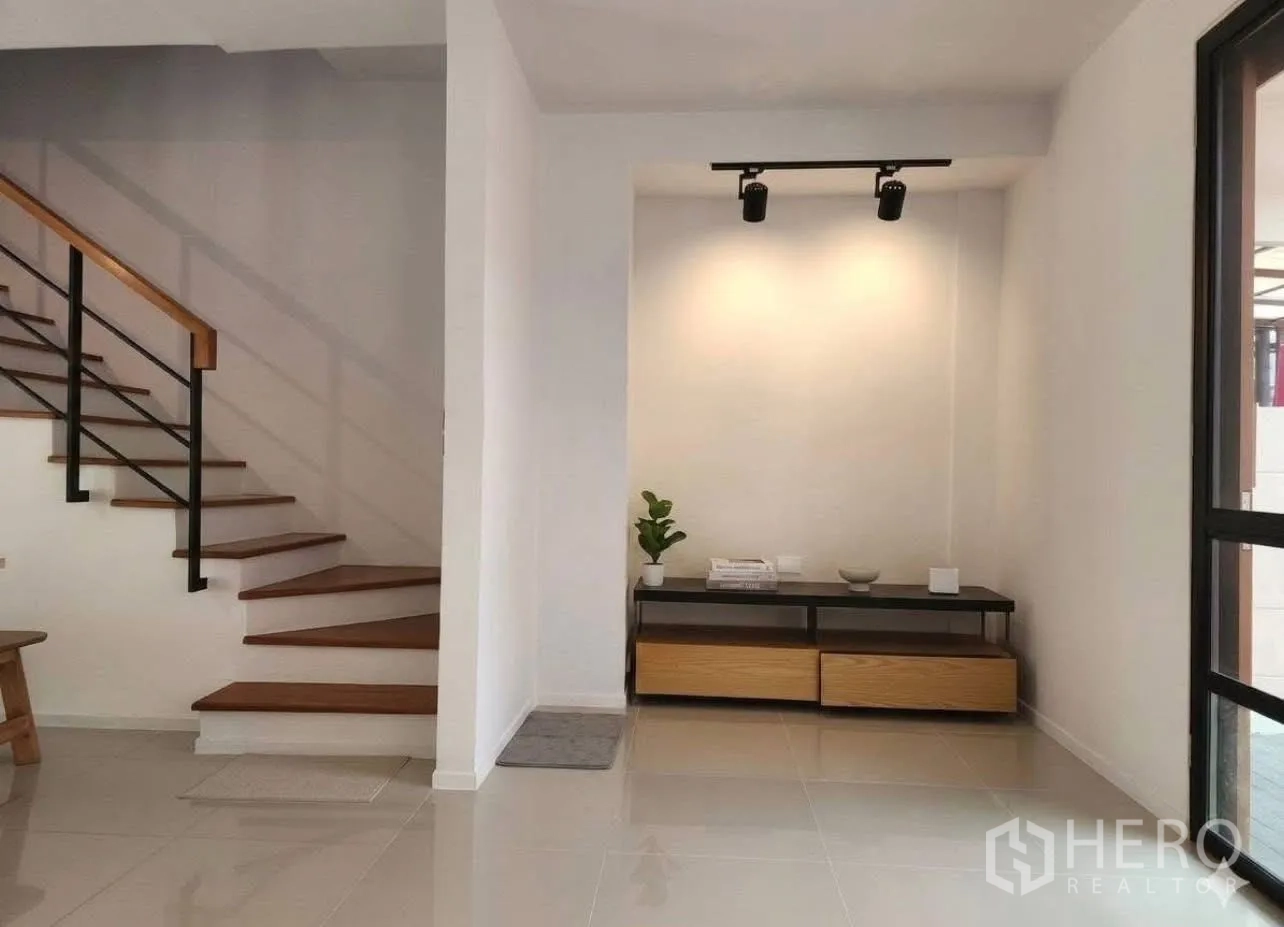 Townhouse for rent in Suan Luang, Bangkok - Entry with wood-tread staircase and a console table under spotlights.