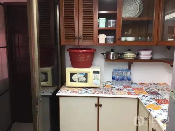 Townhouse for rent in Khlong Toei, Bangkok - Compact kitchen with wooden cabinets, colorful mosaic countertop and microwave.