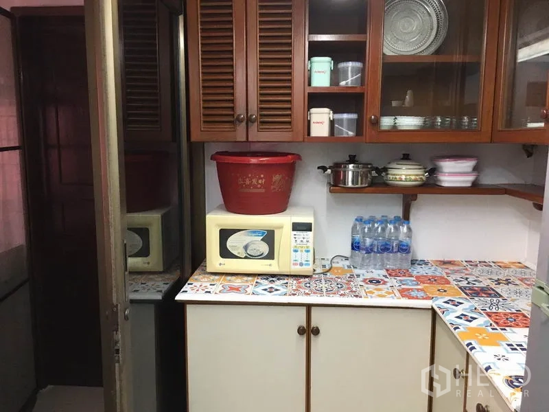 Townhouse for rent in Khlong Toei, Bangkok - Compact kitchen with wooden cabinets, colorful mosaic countertop and microwave.
