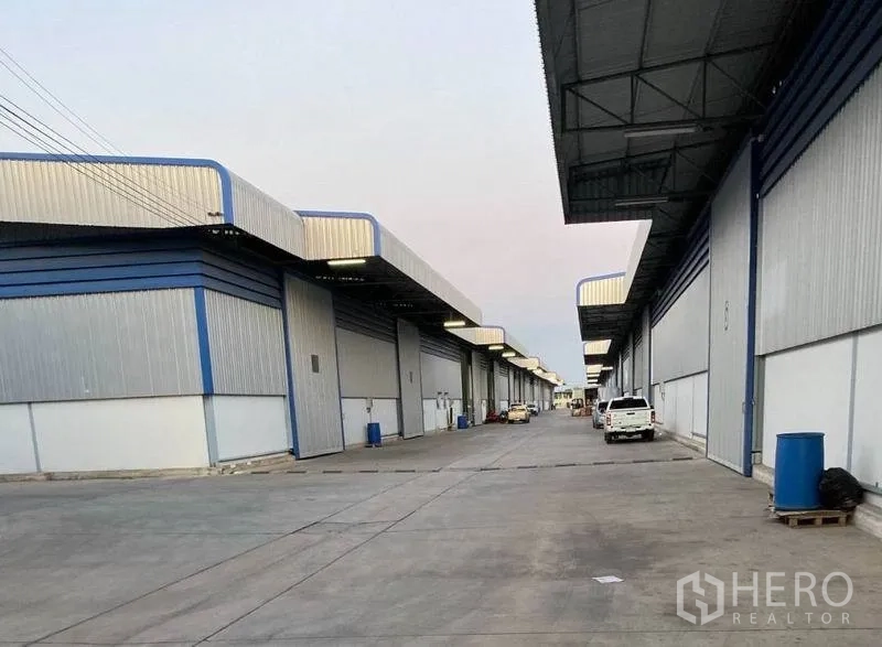 Warehouse for rent in Lat Krabang, Bangkok - Row of warehouse bays with canopies along a concrete access road and parked vehicles.