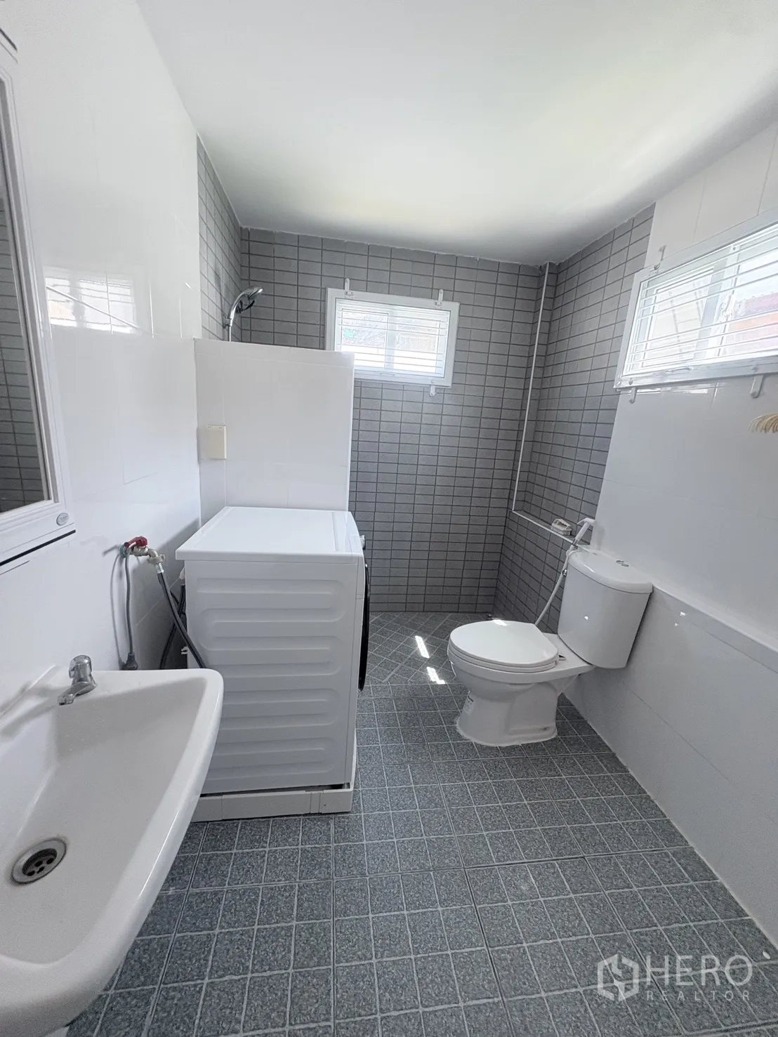 Detached House for rent in Saphan Sung, Bangkok - Bathroom view showing sink, washing machine, toilet, and gray-tiled shower area with windows.