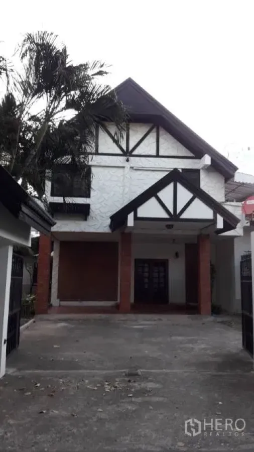 บ้าน ให้เช่าในYan Nawa, Bangkok - ด้านหน้าบ้านสองชั้นหลังคาจั่ว แต่งคานสีดำ มีทางจอดรถและกันสาด ใกล้ต้นปาล์ม