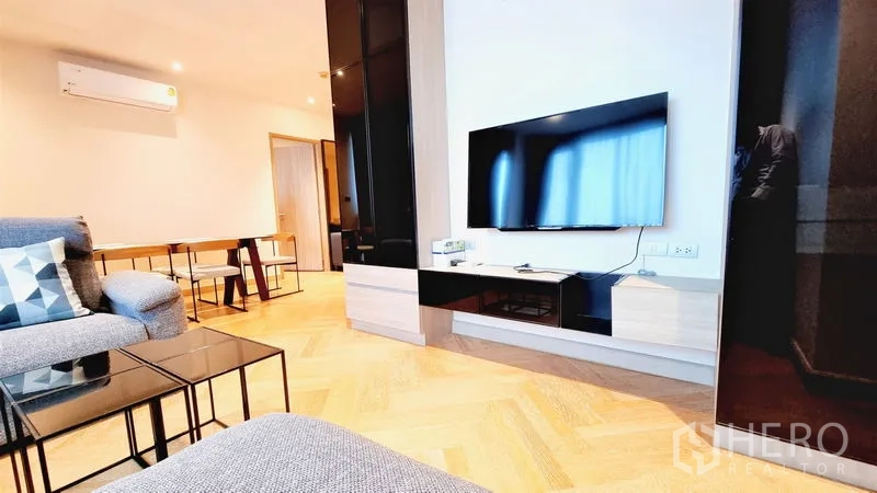 Condominium for sale in Watthana, Bangkok - TV wall with mounted flat-screen, low cabinet and nearby dining set in an open-plan lounge.