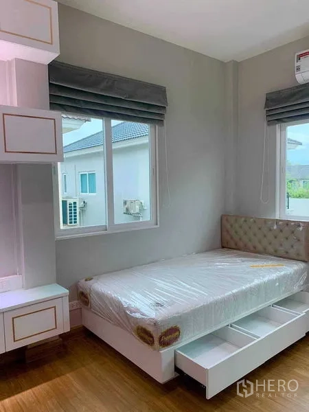 独立式住宅 出租在Bang Khen, Bangkok - 卧室设软包床头、床下抽屉与两扇窗户。