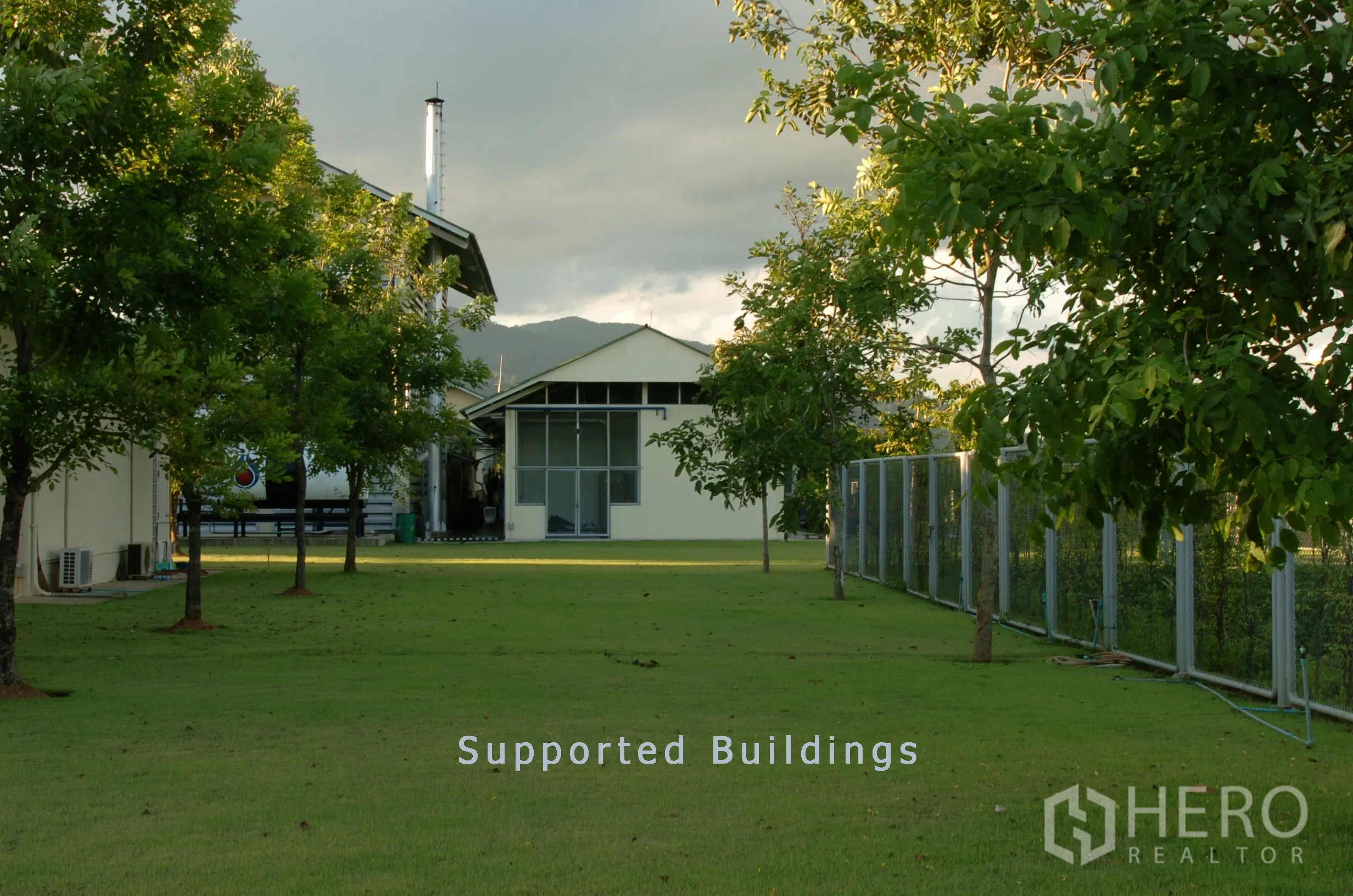 工厂 for sale in Khao Chamao, Rayong - 支援性建筑坐落在草坪与围栏后，远处可见群山。