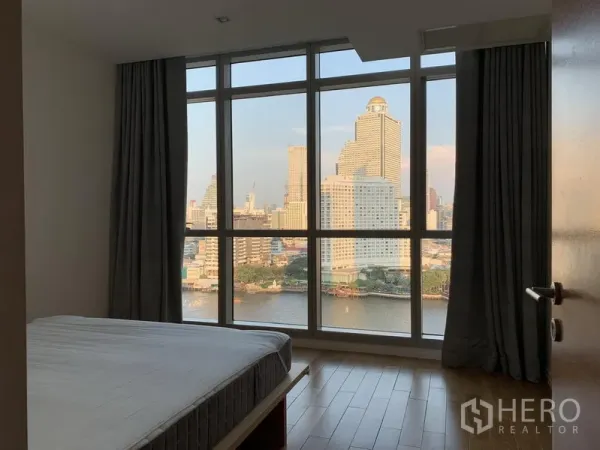 Condominium for rent in Khlong San, Bangkok - Bedroom with full-height windows overlooking the river and cityscape.