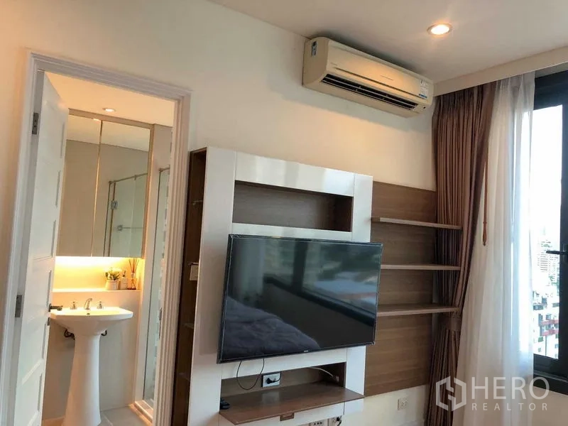 คอนโด ให้เช่า - ผนังทีวีในห้องนอน พร้อมประตูเข้าสู่ห้องน้ำในตัวและเครื่องปรับอากาศ