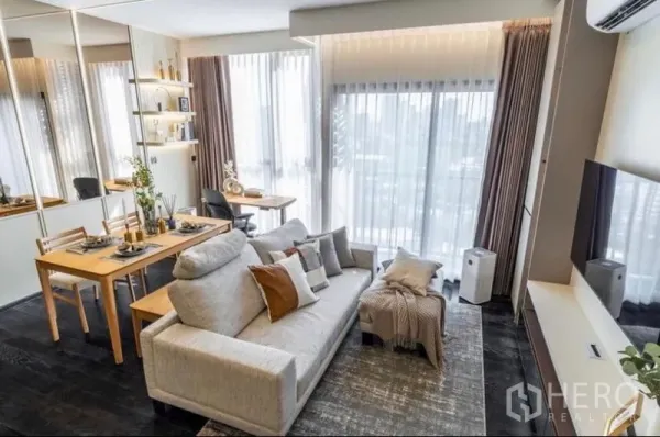 Condominium for sale in Watthana, Bangkok - Cozy lounge with light gray sofa, rug and large glazed doors beside a wooden dining table