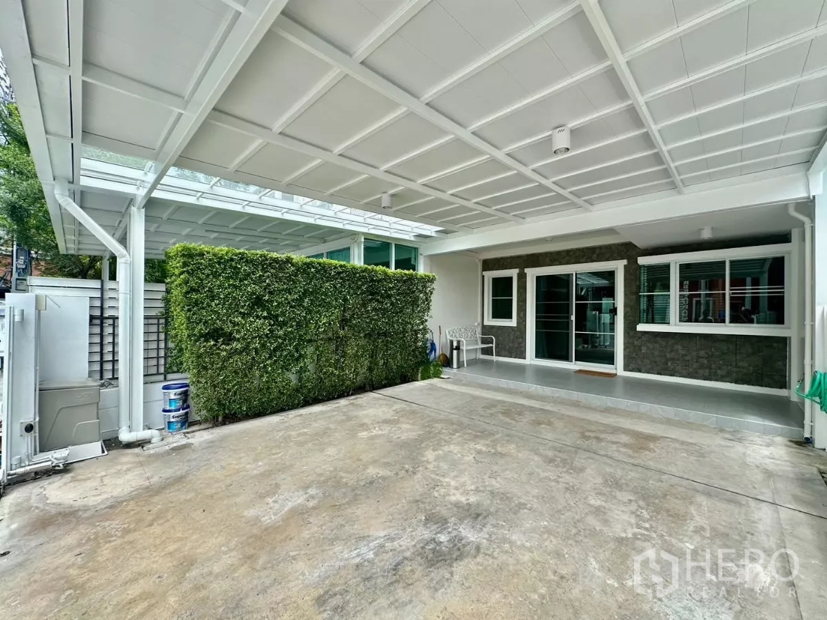 联排别墅 出租在Prawet, Bangkok - 带雨棚的双车位车库，绿篱与玻璃推拉门入口。