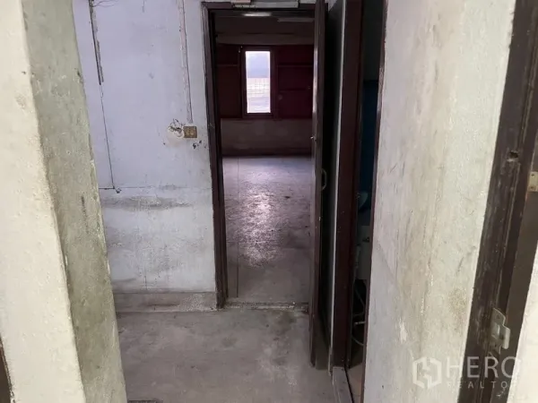 Shophouse for rent in Watthana, Bangkok - Narrow hallway leading to an unfinished room with a single window providing natural light.
