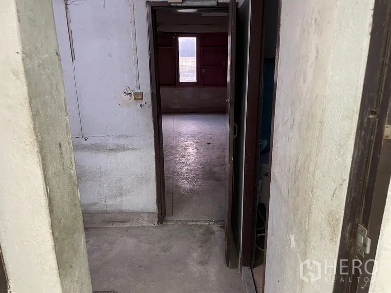 Shophouse for rent in Watthana, Bangkok - Narrow hallway leading to an unfinished room with a single window providing natural light.