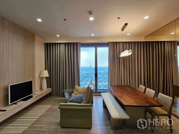 Condominium for rent in Bang Kho Laem, Bangkok - Evening view of living–dining room with TV console, sofa and floor-to-ceiling window over the city.