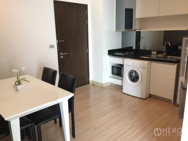 公寓 出租在Watthana, Bangkok - 开放式厨房配黑色花岗岩台面、洗衣机、微波炉与餐桌，木地板的曼谷公寓。