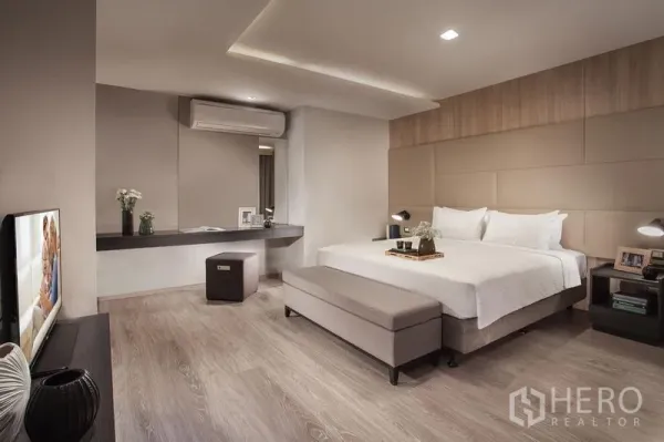 อพาร์ทเมนท์ ให้เช่าในKhlong Toei, Bangkok - ห้องนอนมาสเตอร์กว้าง พร้อมเตียงคิง เฮดบอร์ดบุผ้า ม้านั่งปลายเตียง โต๊ะวางของยาว และเครื่องปรับอากาศ