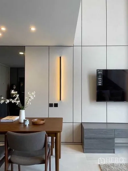 公寓 出租在Pathum Wan, Bangkok - 极简餐桌一角，旁为纵向壁灯与安装在造型墙面的电视。