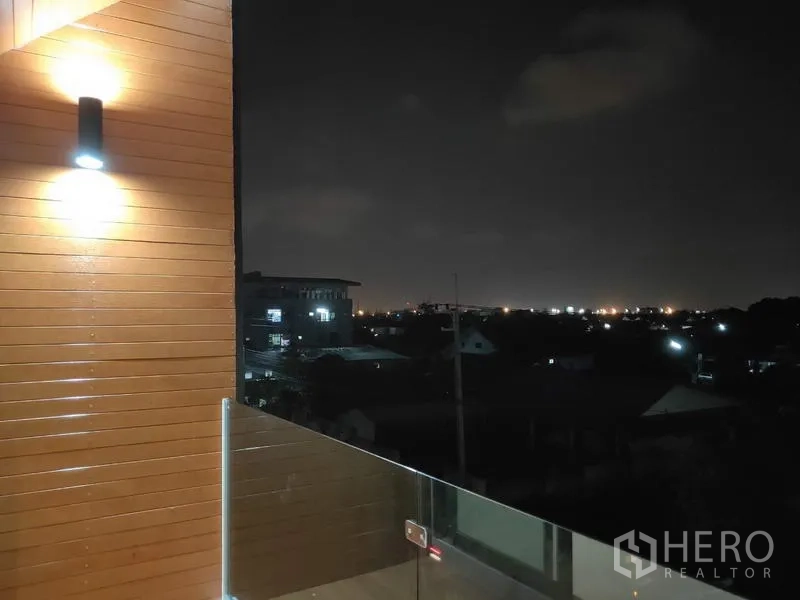 Home Office for sale in Lam Luk Ka, Pathum Thani - Balcony with glass railing and night city view, wall sconce on wood cladding.