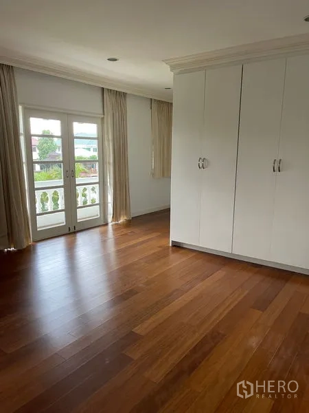 Detached House for rent in Bang Phli, Samut Prakan - Bedroom with warm wood flooring, built-in wardrobe, and French doors to a balcony.