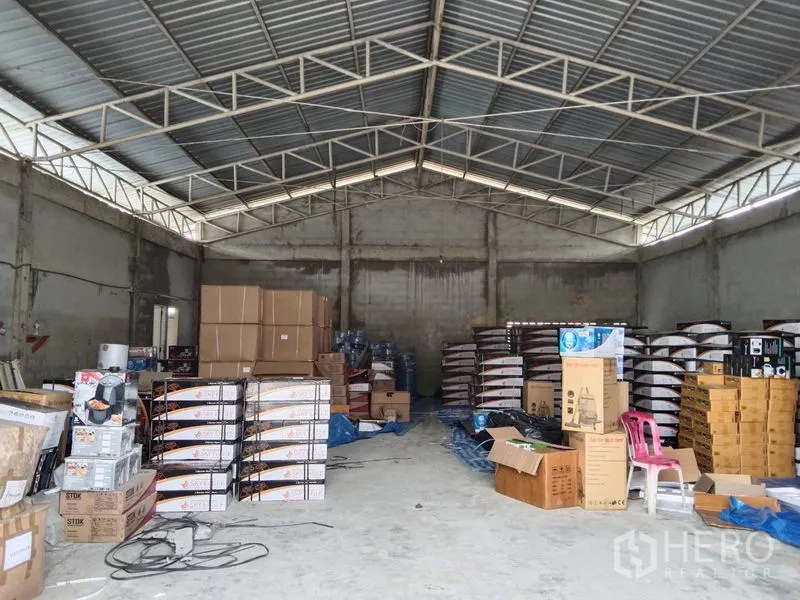 Warehouse for rent in Khlong Sam Wa, Bangkok - Spacious warehouse bay with high ceiling, metal roof trusses and stacks of cartons on the concrete floor.