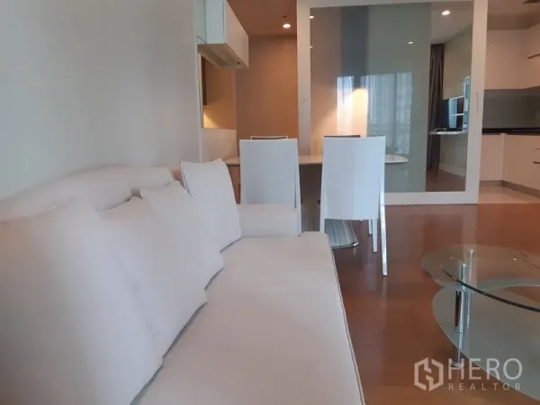 คอนโด ให้เช่าในKhlong Toei, Bangkok - โซนนั่งเล่นแบบเปิด โซฟาสีขาว โต๊ะกระจก ชุดโต๊ะทานอาหาร และผนังกระจกเงาใกล้หน้าต่างบานใหญ่