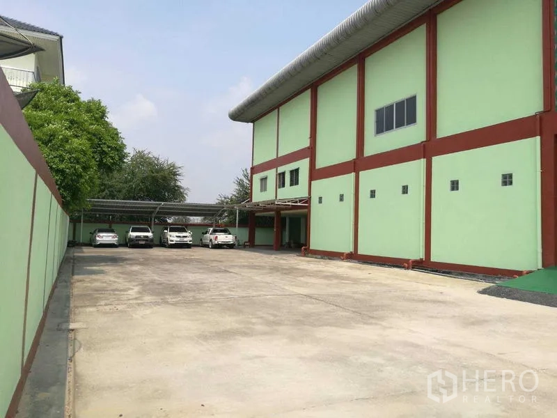 Factory for rent in Mueang Samut Sakhon, Samut Sakhon - Large parking yard with covered carports beside the high warehouse wall.