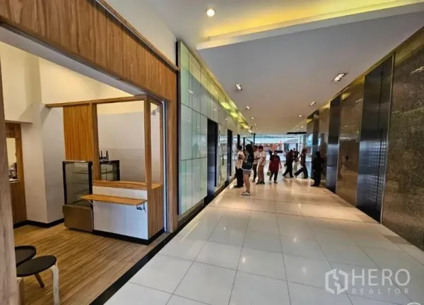 零售空间 出租在Watthana, Bangkok - 大堂走廊，瓷砖地面与多部电梯，左侧为带服务台的店铺门面