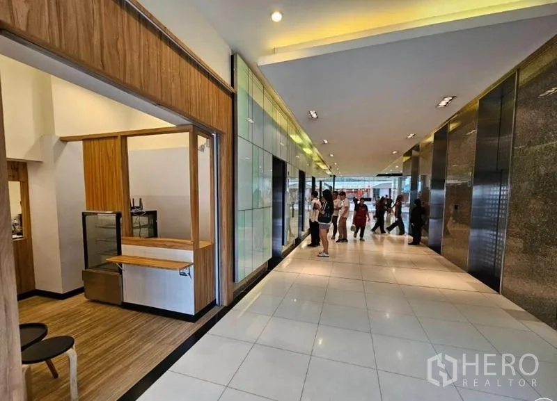 零售空间 出租在Watthana, Bangkok - 大堂走廊，瓷砖地面与多部电梯，左侧为带服务台的店铺门面