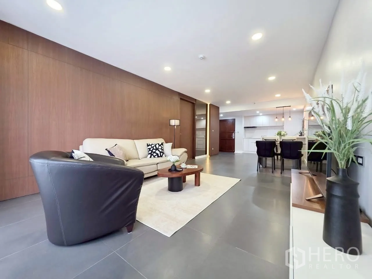 Condominium for rent in Sathon, Bangkok - Open-plan lounge and dining room with wood accent wall and gray tile floors.