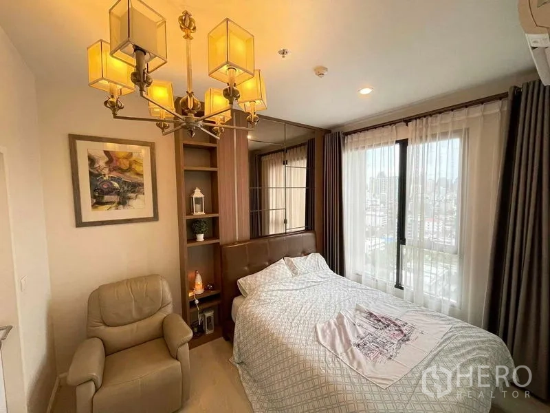 Condominium for sale in Huai Khwang, Bangkok - Bright bedroom with chandelier, large windows, upholstered headboard and city view.