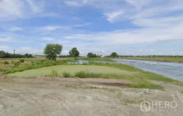 Land for sale in Chachoengsao - Small green pond and a long waterway with a lone tree on flat farmland.