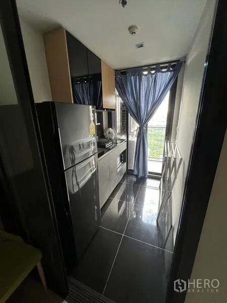 公寓 出租在Chatuchak, Bangkok - 狭长厨房，亮面地砖、冰箱，并可通往阳台的门帘。