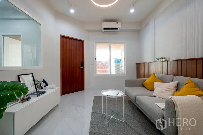 Townhouse for sale in Din Daeng, Bangkok - Air-conditioned lounge with grey sofa, white console and wood entry door.