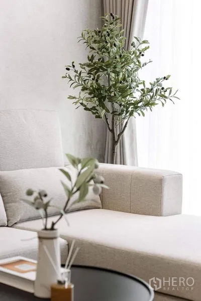 公寓 出租在Bang Rak, Bangkok - 米色转角沙发细节，旁置绿植与轻薄窗帘。