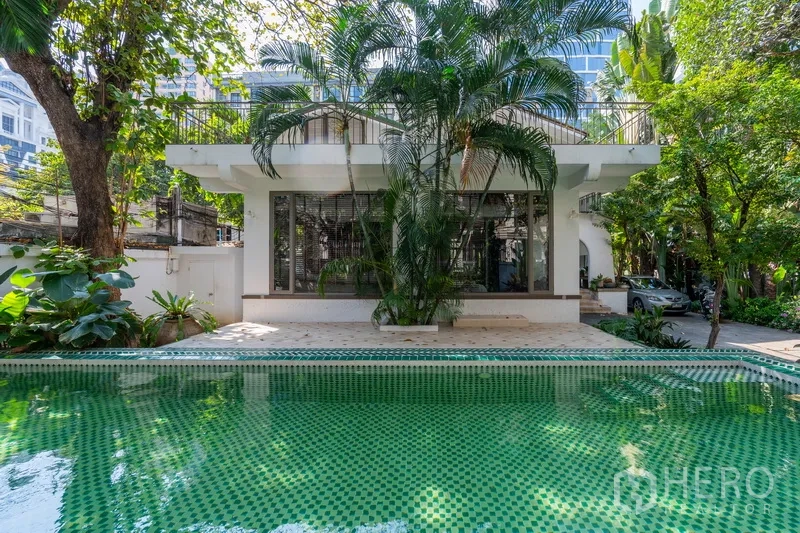 Detached House for rent in Pathum Wan, Bangkok - Private green‑tiled swimming pool beside tropical garden and modern white facade.