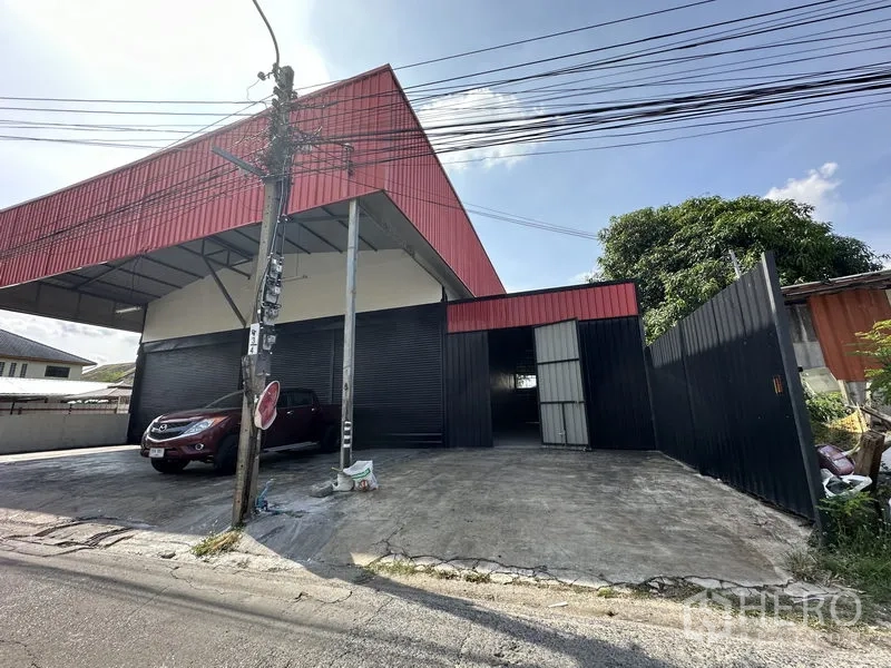 คลังสินค้า ให้เช่าในLat Phrao, Bangkok - มุมมองด้านข้างโกดังพร้อมประตูรั้วทางเข้า รั้วเหล็กสีดำ และลานคอนกรีตกว้าง