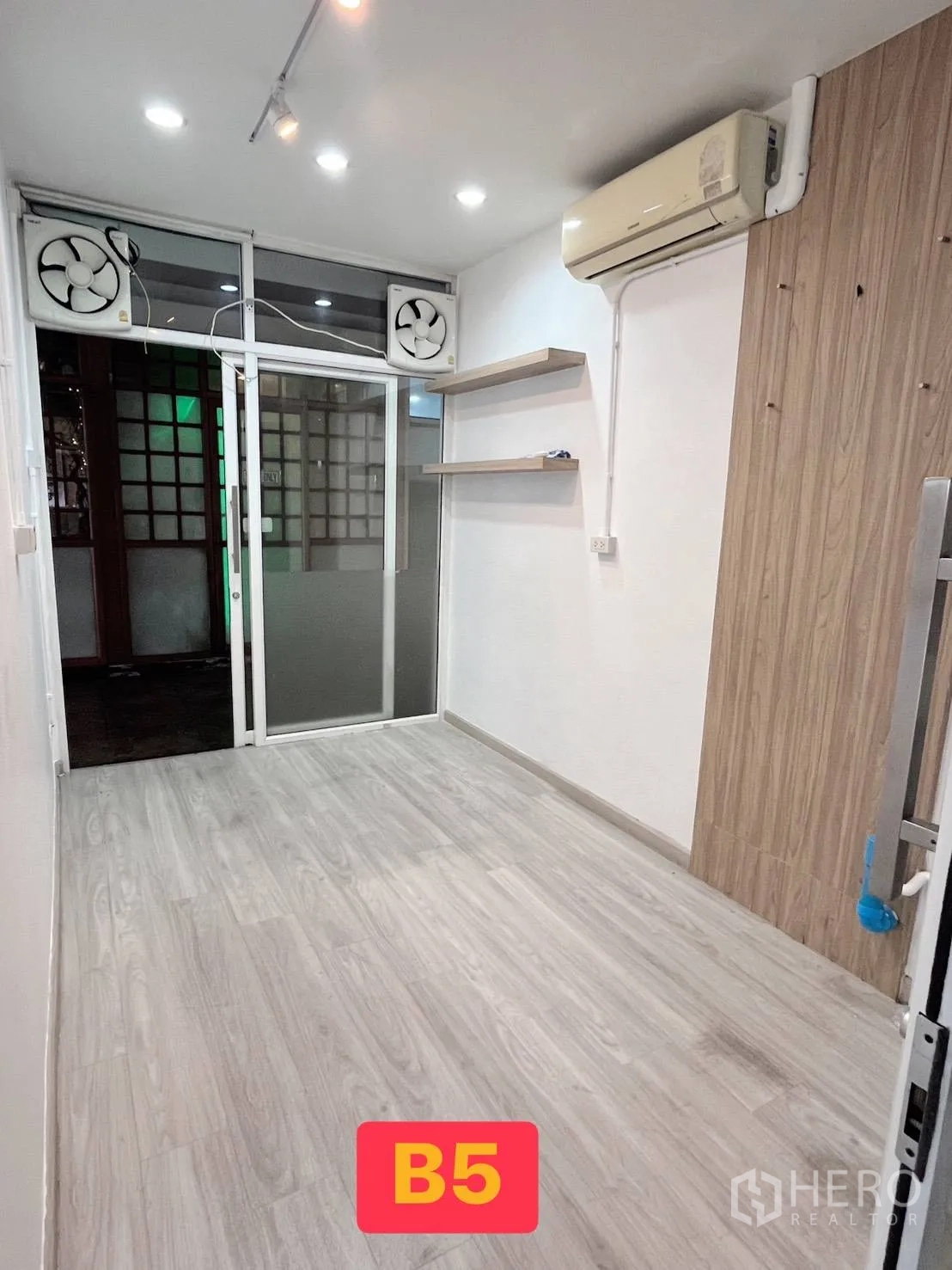 Retail Space for rent in Watthana, Bangkok - Retail room with floating shelves, track lights, wall-mounted AC, and a glass door framed by ventilation fans.