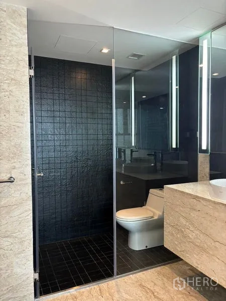 Condominium for rent - Bathroom zone with glass-enclosed toilet and black tiled wall.