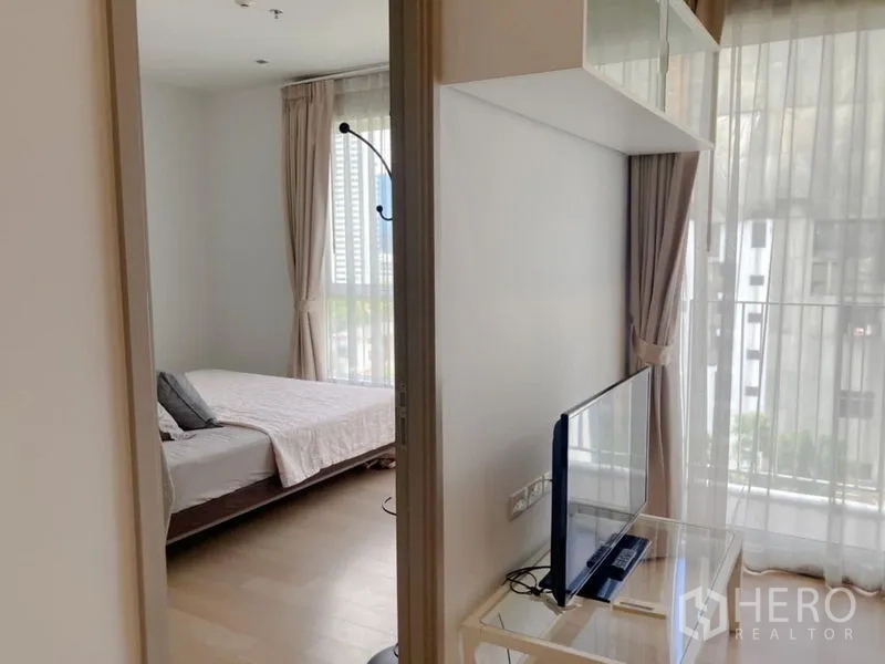 Condominium for rent in Watthana, Bangkok - View from living room to bedroom with floor-to-ceiling windows and a compact TV stand.