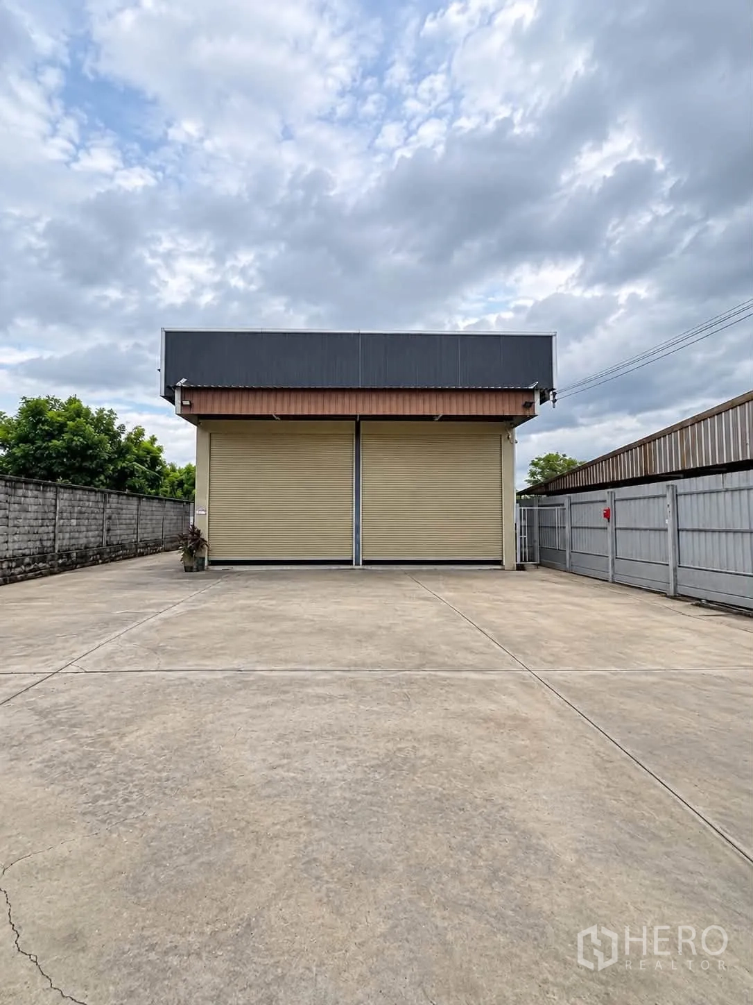 Warehouse for rent in Bang Kruai, Nonthaburi - Warehouse facade with twin roller shutters and a large gated concrete yard enclosed by walls.