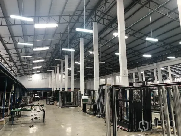 Warehouse for rent in Nonthaburi - Bright industrial hall showing steel trusses, suspended lights and organized work zones.