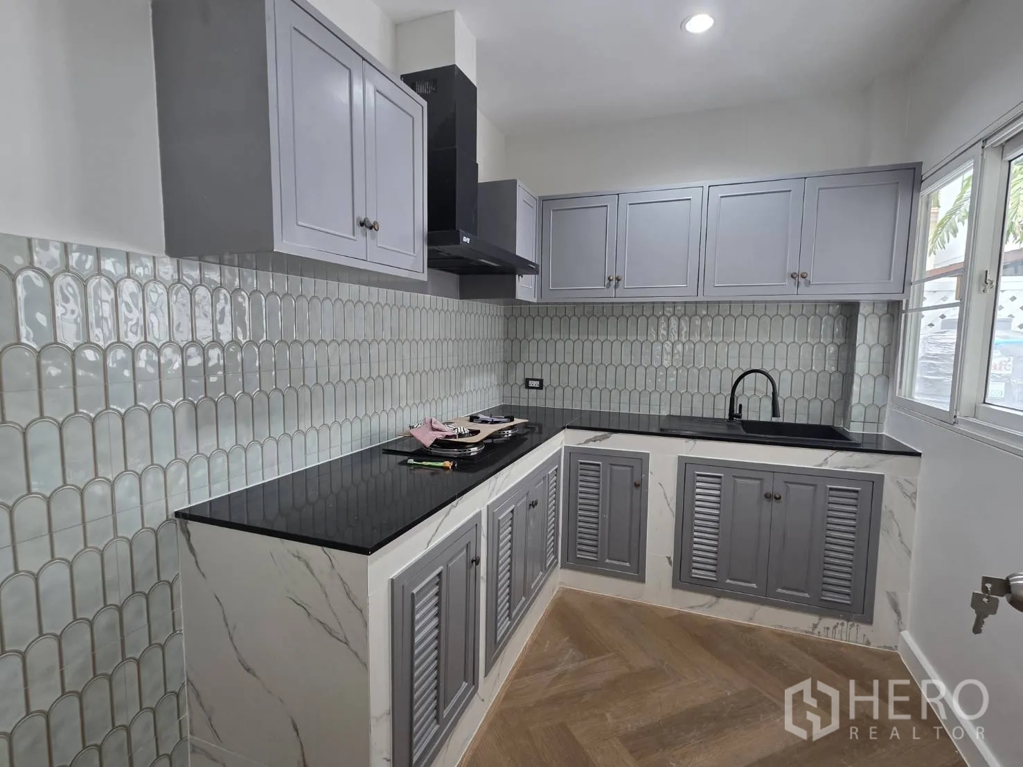 Detached House for sale in Lam Luk Ka, Pathum Thani - U-shaped kitchen with grey shaker cabinets, black countertops, tiled backsplash, and window.