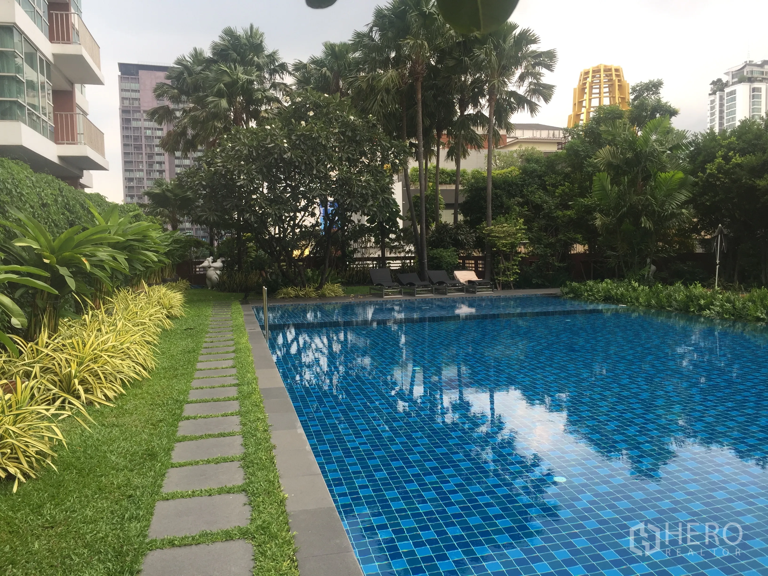 Condominium for rent or sale in Watthana, Bangkok - Outdoor lap pool with blue tiles surrounded by lush tropical garden at a Watthana condominium.