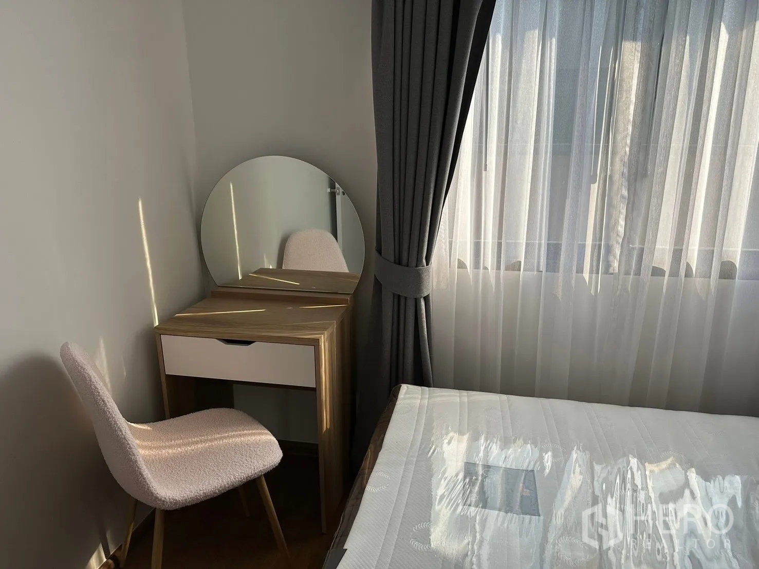 ทาวน์เฮาส์ for rent in Bang Phli, Samut Prakan - มุมห้องนอนแสงธรรมชาติ โต๊ะเครื่องแป้งกระจกกลม เก้าอี้บุผ้า และม่านสองชั้นข้างเตียง