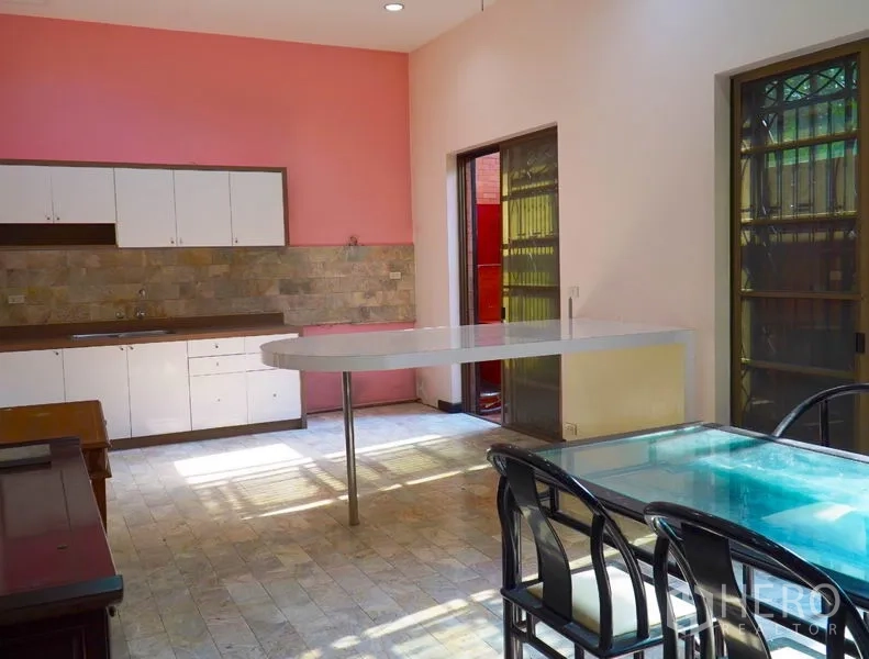 Townhouse for rent in Pathum Wan, Bangkok - Bright kitchen-dining room with pink wall, cabinets and an island.