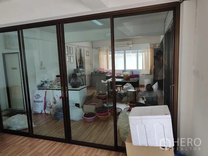 工厂 出售在Sai Noi, Nonthaburi - 玻璃隔断办公室，木地板上摆放办公桌与物资。