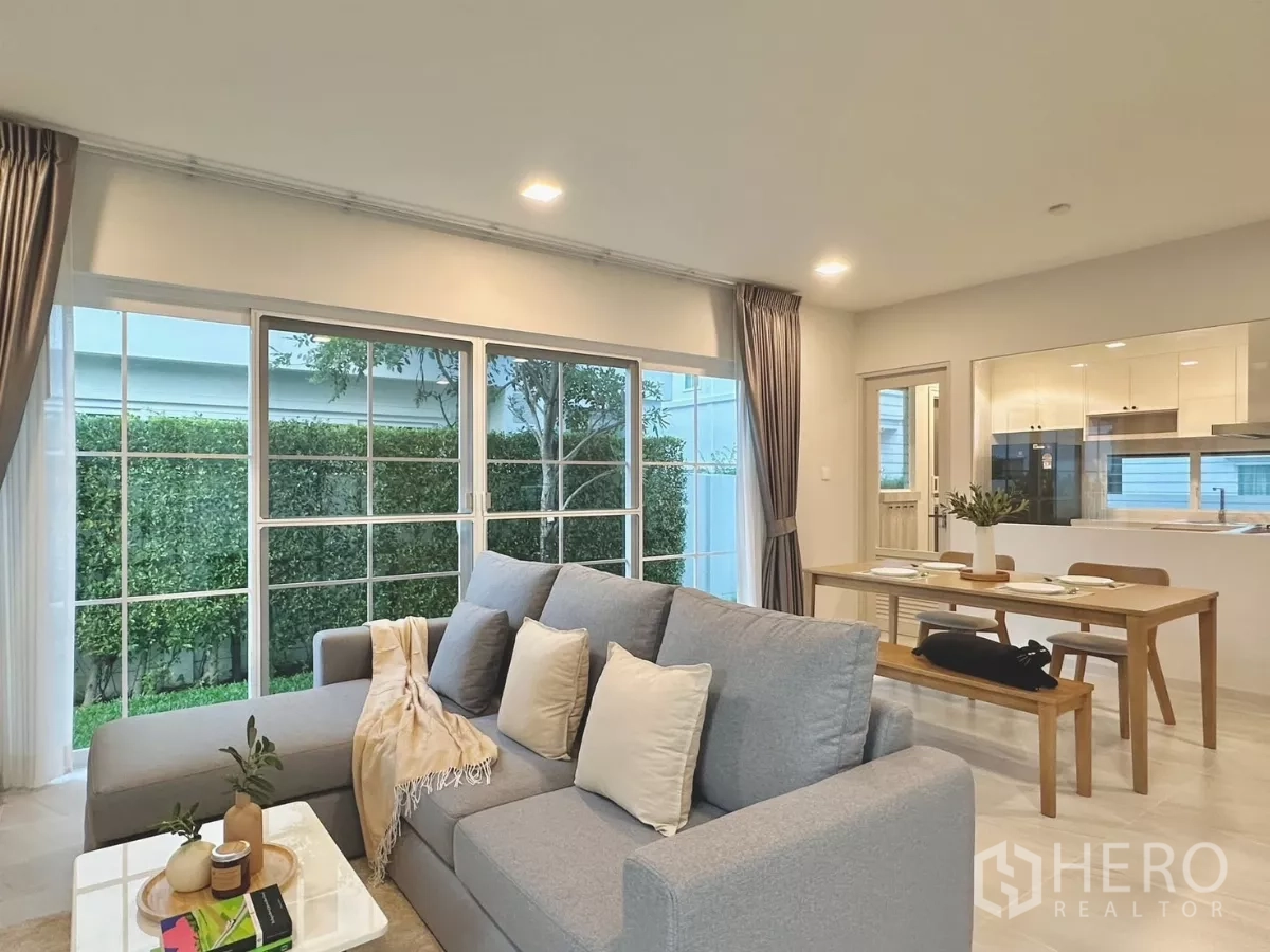 独立式住宅 出租在Bang Phli, Samut Prakan - 客厅设灰色转角沙发，临窗而坐，毗邻餐区与厨房。