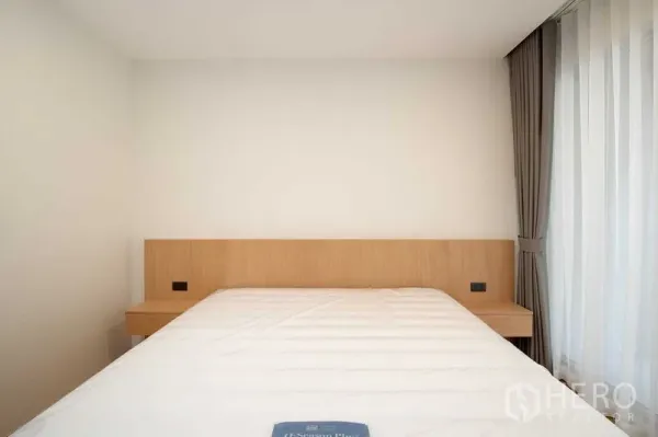 Condominium for rent in Phra Khanong, Bangkok - Minimalist bedroom with light wood headboard, white bedding and full-height curtains.