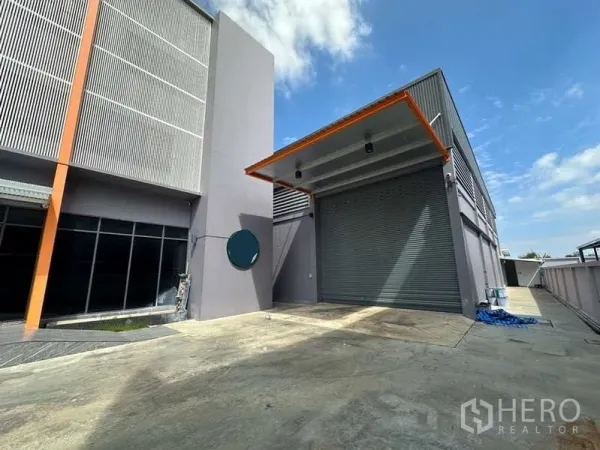 Factory for rent in Lam Luk Ka, Pathum Thani - Covered loading bay with roller shutter door and wide concrete apron beside the office block.